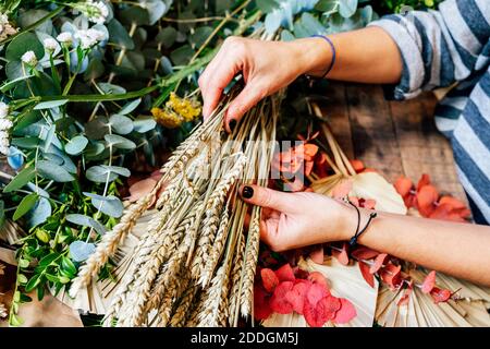 D'en haut, une femelle fleuriste professionnelle inreconnaissable organise un bouquet de fleurs en travaillant en atelier sur une table en bois Banque D'Images