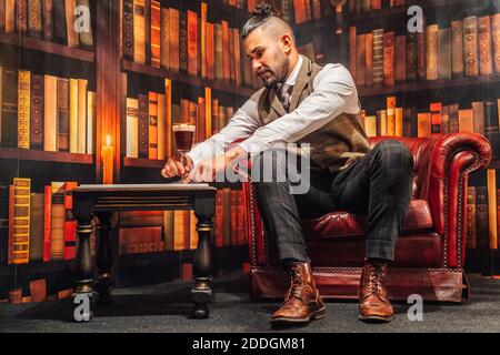Corps complet de l'homme dans un élégant costume tenant le verre de Café irlandais dans un fauteuil confortable Banque D'Images