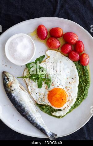 D'œufs frits au-dessus, servis avec du poisson salé et marinés tomates et garniture de sauce pesto Banque D'Images