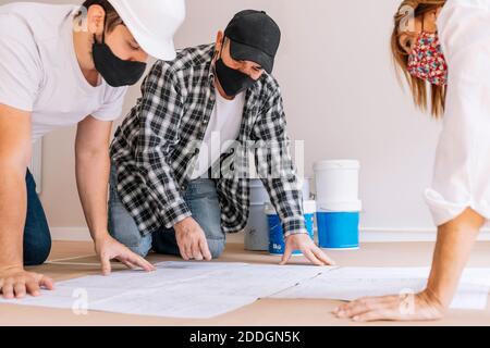 Compagnie de personnes dans les masques de protection lisant les brouillons de papier et préparation pour la rénovation et la peinture dans une salle lumineuse Banque D'Images
