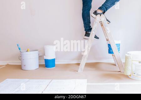 Crop anonyme homme peintre debout sur l'échelle en bois et la rénovation intérieur de la chambre Banque D'Images