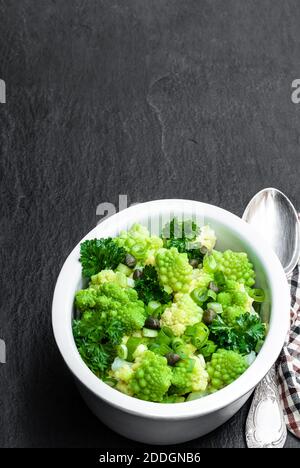 Chou-fleur romanesco avec câpres et salade d'oignons sur pierre noire arrière-plan Banque D'Images