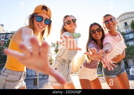 Groupe d'amis du millénaire moderne dans des tenues et des lunettes de soleil qui dépassent les bras et regardent l'appareil photo tout en profitant de l'été en ville Banque D'Images