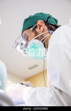 Faible angle du dentiste mâle concentré dans les lunettes binoculaires et uniforme travaillant dans une clinique dentaire moderne Banque D'Images