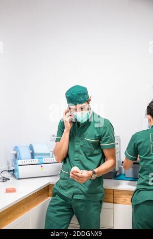 Dentiste masculin en masque et uniforme parlant sur smartphone pendant tenir le plâtre dentaire dans l'hôpital dentaire moderne Banque D'Images