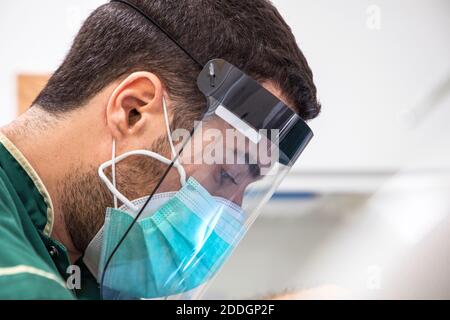 Vue latérale d'un médecin masculin avec masque et visage protéger pendant le travail Banque D'Images