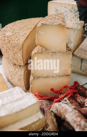 Divers types de savoureux fromages artisanaux aromatiques placés près de la viande saucisses au comptoir du marché agricole local Banque D'Images