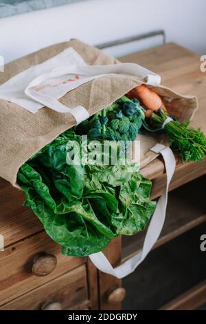 Sac en papier avec feuilles vertes placé sur le comptoir en bois avec brocoli frais et bouquet de carottes du marché agricole Banque D'Images