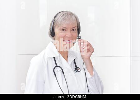 Sympathique médecin senior pendant une consultation en ligne comme vu par une webcam, fond blanc, copyspace. Banque D'Images