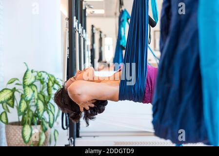 Vue rapprochée latérale de la posture du bateau de la femme silks aériens pendant la leçon de yoga dans la salle de sport moderne Banque D'Images