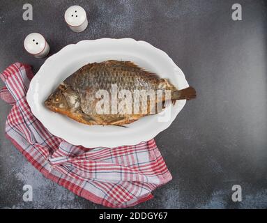 Carpe de poisson grillée sur une assiette blanche sur fond sombre. Banque D'Images