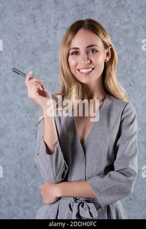 Jeune femme d'affaires blonde portant un costume gris et tenant un stylo. Banque D'Images