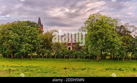 Paysage panoramique avec un palais Plawniowice au milieu d'arbres avec un ciel de soleil coloré sur lui et des verts en face. Banque D'Images