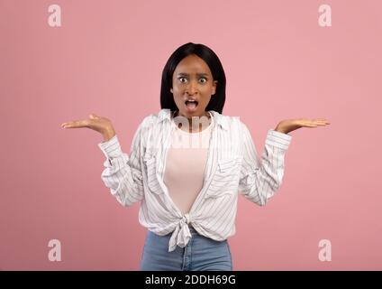 Une femme afro-américaine agacée qui se fait le gestier, se haussant les épaules sur fond de studio rose Banque D'Images