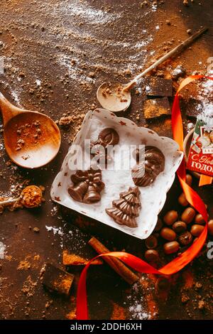 Noël chocolat chiffres Santa Claus, arbre de Noël, cloches, bougie sont sur la table sombre à côté d'une barre de chocolat avec de l'orange et des épices Banque D'Images