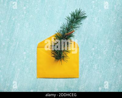 Composition de Noël ou du nouvel an. Enveloppe jaune en papier avec branche d'épinette sur fond bleu. Style de pose à plat. Carte de vœux du nouvel an. Banque D'Images