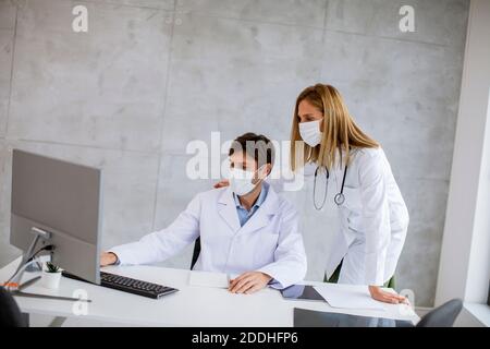 Médecins de couple avec des masques médicaux de protection du visage parlant et utilisation de l'ordinateur dans l'image Banque D'Images