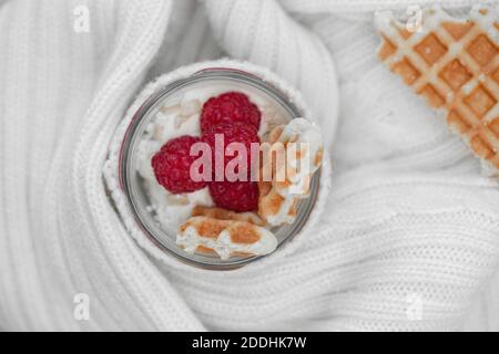 Fromage cottage avec framboises, muesli et gaufres, sur le yaourt dans un pot enveloppé dans un chandail blanc chaud. Banque D'Images