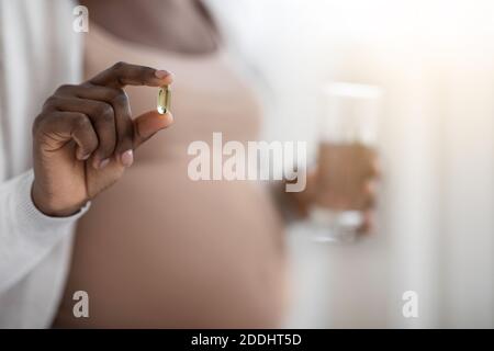 Suppléments de grossesse. Femme enceinte noire tenant une capsule de vitamine et un verre d'eau Banque D'Images