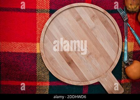 Fond pour la cuisson ou la cuisson au froid : plateau de coupe en bambou en bois rond et vide sur un tissu à damier avec des fruits Banque D'Images