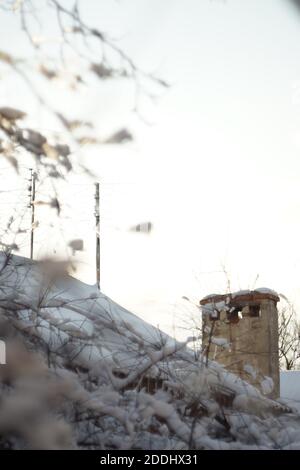 Cheminée rurale et antennes sur un toit couvert de neige et branches de l'arbre Banque D'Images
