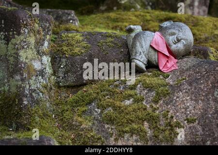 Gros plan horizontal d'une statue en pierre souriante de Jizo qui se dresse au-dessus d'un rocher dans le temple bouddhiste de Daisho-in, Miyajima, Japon Banque D'Images