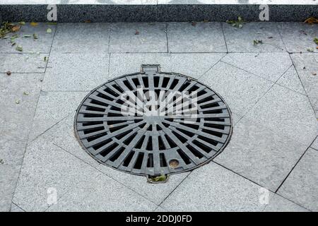 couverture de trou d'homme rond treillis de métal noir de l'amélioration ville trottoir piétonnier pavé avec carreaux gris de granit vue rapprochée, personne. Banque D'Images