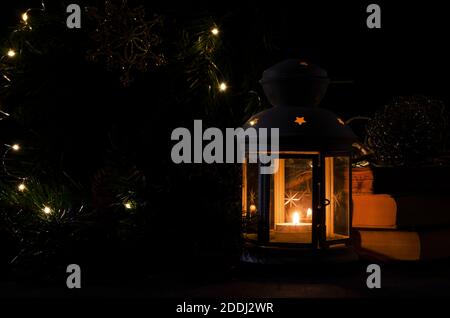 Lanterne blanche avec une bougie allumée. Livres, branche d'arbre de Noël et lumières sur fond. Image sombre de nuit. Humeur mystère de Noël. Banque D'Images