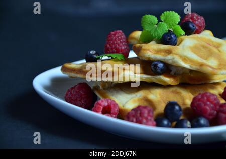 Gaufres belges faites maison avec myrtilles fraîches pour le petit-déjeuner. Assiette blanche, gaufres viennoises avec framboises et menthe. Petit déjeuner délicieux et rapide sur le b Banque D'Images