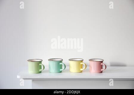 Quatre petites tasses à café pastel multicolores sur une console blanche contre un fond de mur. Copier l'espace. Placer pour le texte Banque D'Images