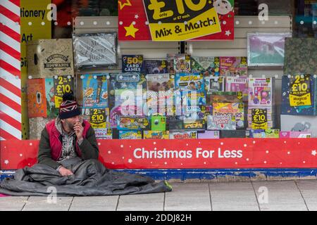 homme sans abri assis sur le sol ou le trottoir à l'extérieur d'un magasin vendant des articles de noël. Banque D'Images