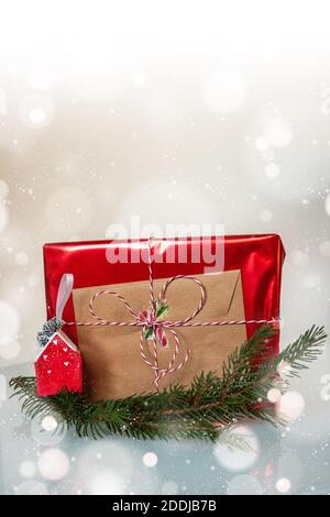 Des articles de fête pour savourer tous les cadeaux de Noël. Brindilles de pin doré et de sapin vert de classe associées à un ornement fait main en forme de maison. Emballage rouge brillant Banque D'Images