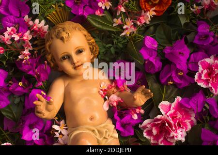 Vieille figurine de l'enfant de Noël Jésus entouré de fleurs de différentes variétés Banque D'Images