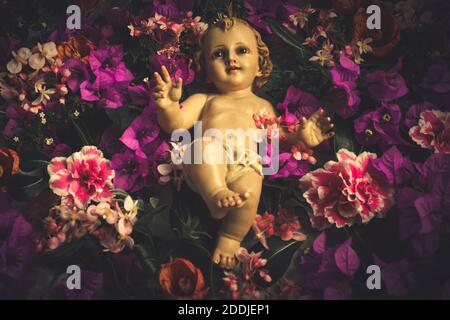 Religion de Noël carte de voeux catholique.ancienne figurine de l'enfant Jésus sur un fond de fleurs, bougainvilliers et azalées style vintage Banque D'Images