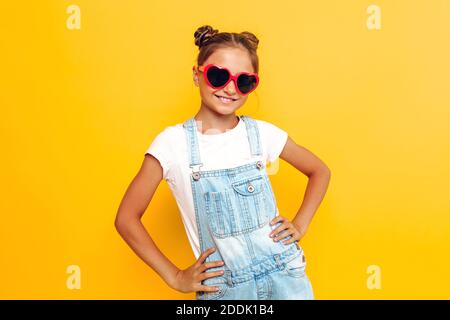 Adolescent élégant avec des verres en forme de coeur, fille heureuse posant sur fond jaune Banque D'Images