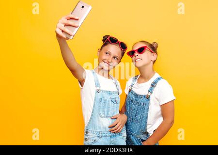 Deux adolescentes en lunettes de soleil se reposent et prennent un selfie sur un smartphone sur un fond jaune. Banque D'Images