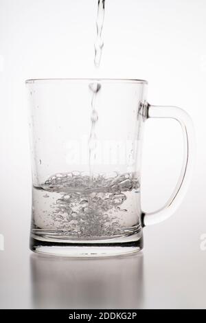 Verser de l'eau dans une tasse. Récipient en verre pour alcool faiblement carbonaté. Arrière-plan clair. Banque D'Images