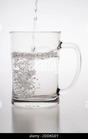 Verser de l'eau dans une tasse. Récipient en verre pour alcool faiblement carbonaté. Arrière-plan clair. Banque D'Images