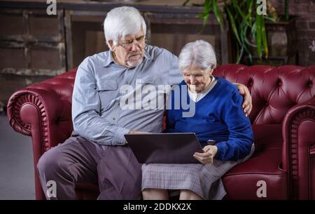 Homme mature et femme âgée utilisant un ordinateur portable tout en étant assis sur un canapé. Passer des appels vidéo, regarder des vidéos ou surfer sur le Web sur un ordinateur portable. Banque D'Images