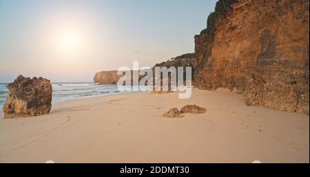 Lumière du soleil au-dessus de la plage de paradis tropical avec sable blanc et eau de l'océan propre cristal. Antenne de la falaise au bord de la baie de mer avec pierres, rochers. Lumière douce du soleil sur la côte rocheuse de l'île de Sumba, en Indonésie Banque D'Images