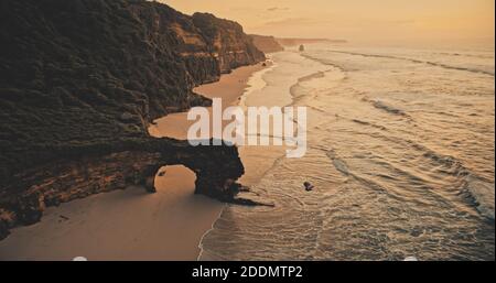 Coucher de soleil sur le mur de rochers sur la plage de sable vue aérienne. Personne de paysage de mer de nature avec des vagues le soir d'été. Paysage incroyable sur la falaise. Lumière douce scène cinématographique soleil Indonésie Banque D'Images