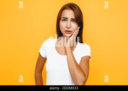 Une fille souffrant de maux de dents douloureux, frognant et touchant sa joue, étant mécontenté, debout avec la douleur sur un fond jaune Banque D'Images