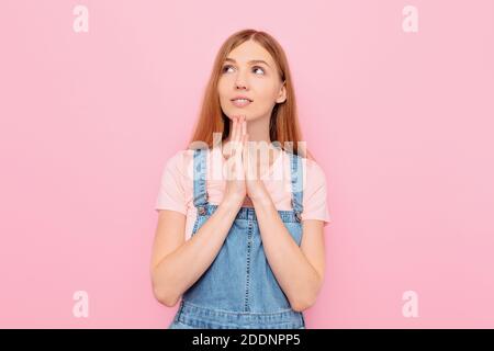 Une jeune belle fille gaie avec espoir prie sur un arrière-plan rose isolé Banque D'Images