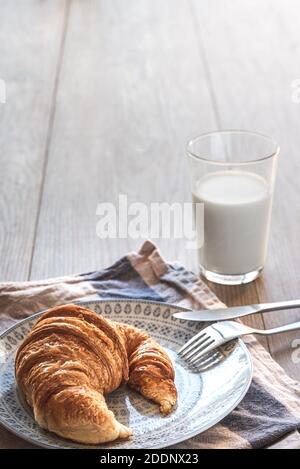 vue verticale d'un croissant traditionnel sur une assiette avec une serviette blanche et bleue et sur une table en bois avec un verre de lait sur le fond. Banque D'Images