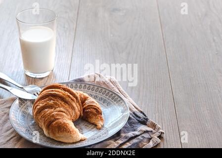 vue horizontale d'un croissant traditionnel sur une assiette avec une serviette blanche et bleue et sur un bois table avec un verre de lait avec une boisson s Banque D'Images