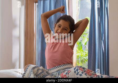 Jeune fille assise sur le lit s'étirant tôt le matin heures de la journée Banque D'Images