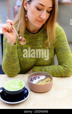 Bol à smoothie de nourriture crue et de matcha Latte coupe de thé vert sur la table et une femme prête à manger. Photo verticale Banque D'Images