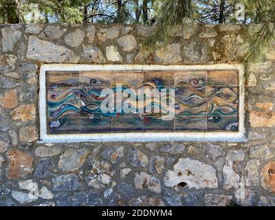 Art mural en verre et peinture sur un mur extérieur en pierre. Sol en pierre et pins à l'arrière-plan. Motif vagues et eau. Banque D'Images