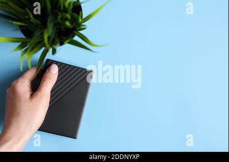 le disque dur externe est noir dans la main femelle et une plante verte sur fond bleu. espace pour le texte Banque D'Images