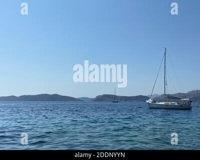 Voile sur les eaux bleu turquoise de la mer Égée. Yacht blanc dans la baie et les îles à l'horizon. Ciel bleu clair. Banque D'Images